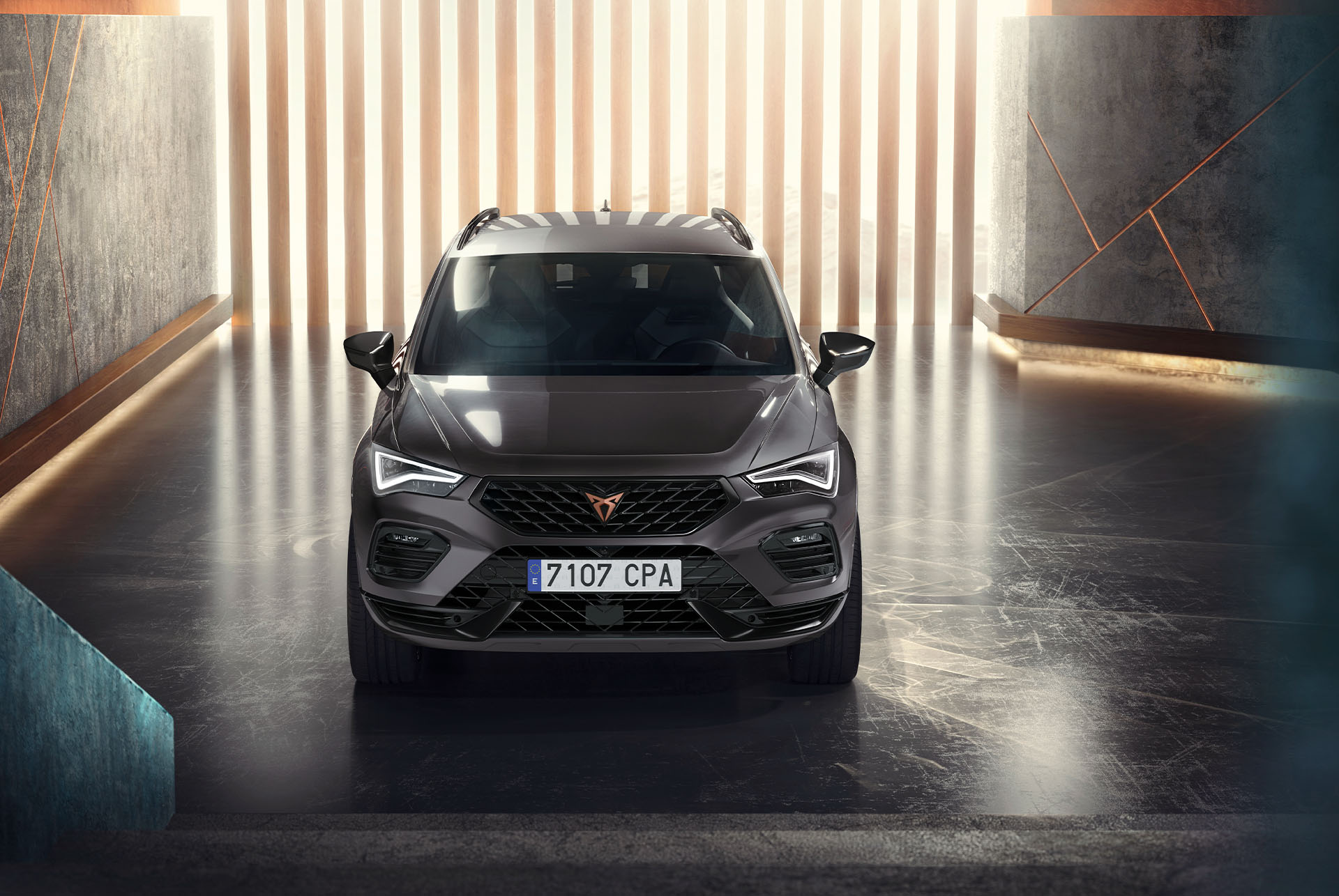 Vista frontal del CUPRA Ateca, un SUV de color gris, en un ambient modern i il·luminat. La imatge destaca la graella frontal atrevida del cotxe, els fars LED i el seu disseny aerodinàmic.