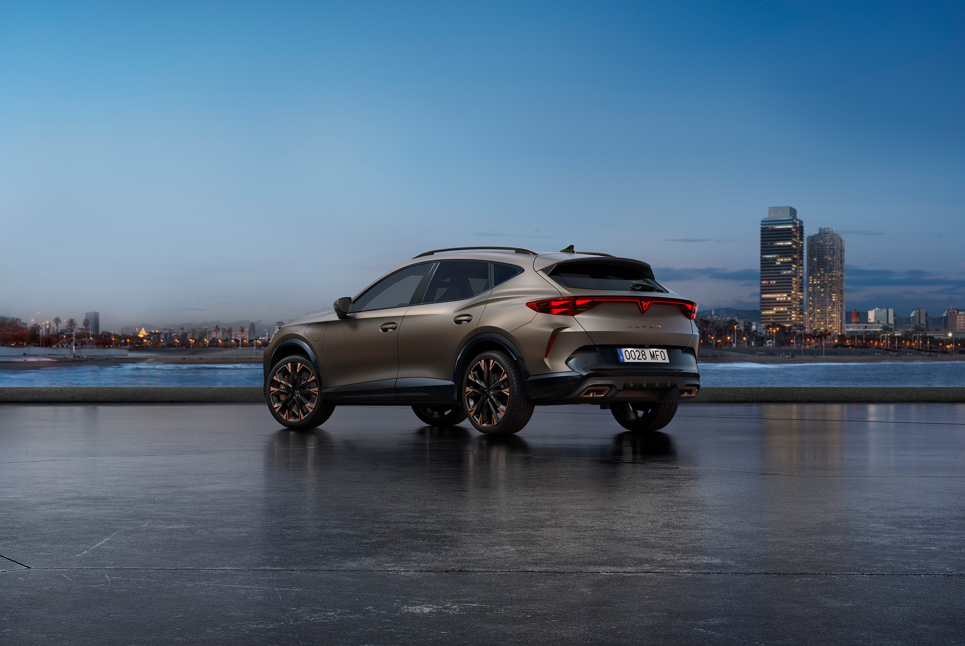Cupra Formentor 2025, color Bronze century, vistra de tres quarts posterior exterior. El nou Cupra Formentor estacionat envoltat d'una arquitectura futurista i de l'horitzó de la ciutat, mostrant el seu disseny posterior i les seves llums.