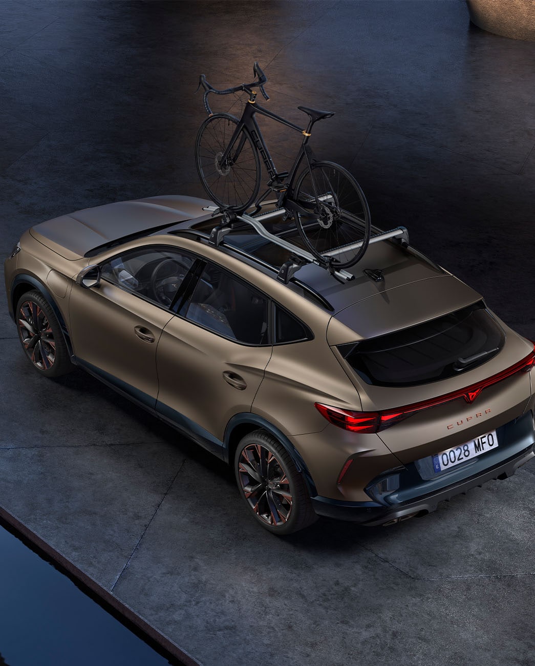 Vista d'ocell del CUPRA Formentor 2025 bronze century mat amb accessori portabicicletes, cotxe aparcat sobre ciment al capvespre.