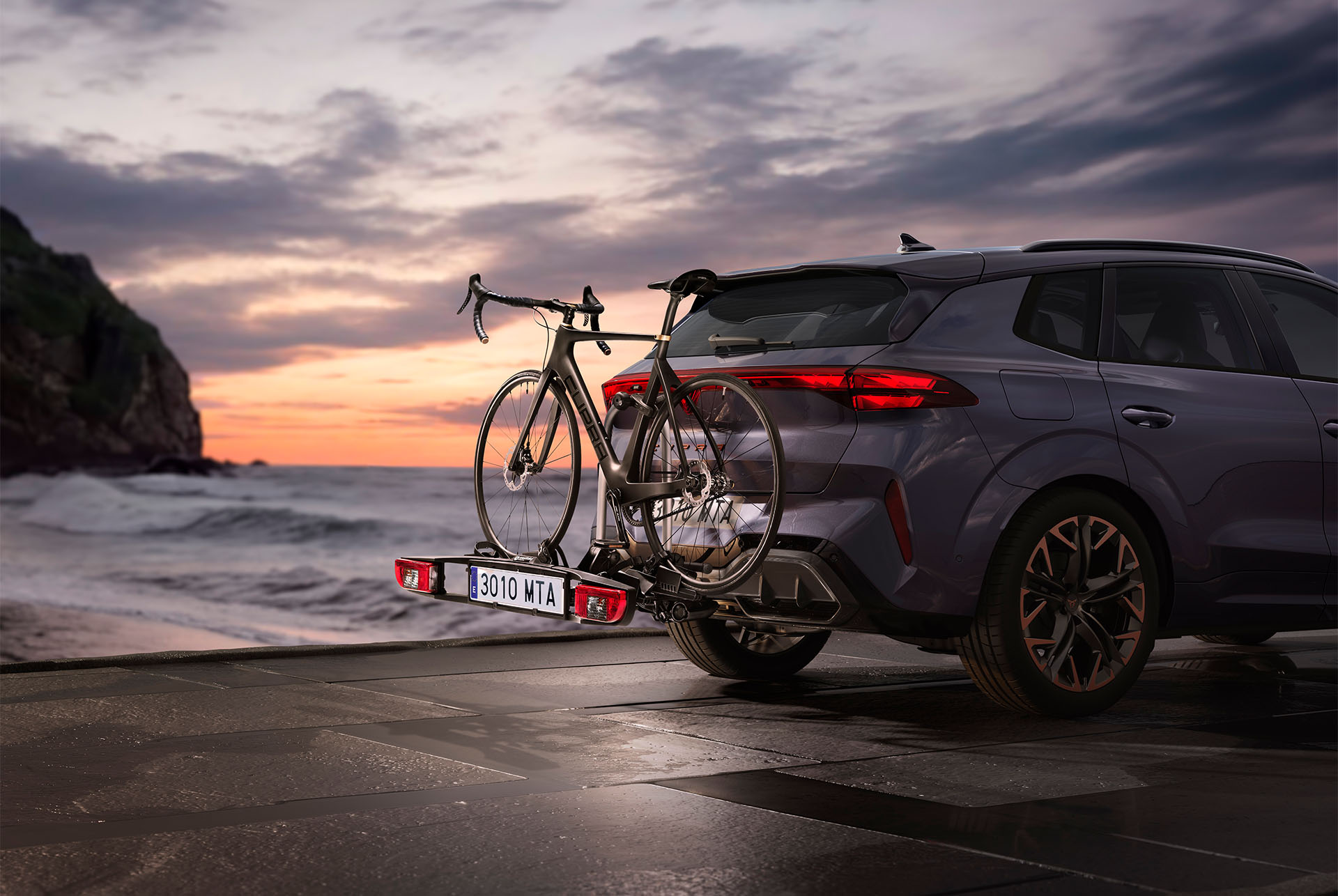Portabicicletes CUPRA amb barra de remolc i dues bicicletes fixades, estacionat a la costa al capvespre. El suport de remolc ofereix una opció còmoda i segura per transportar bicicletes, amb una capacitat de càrrega de fins a 60 kg.