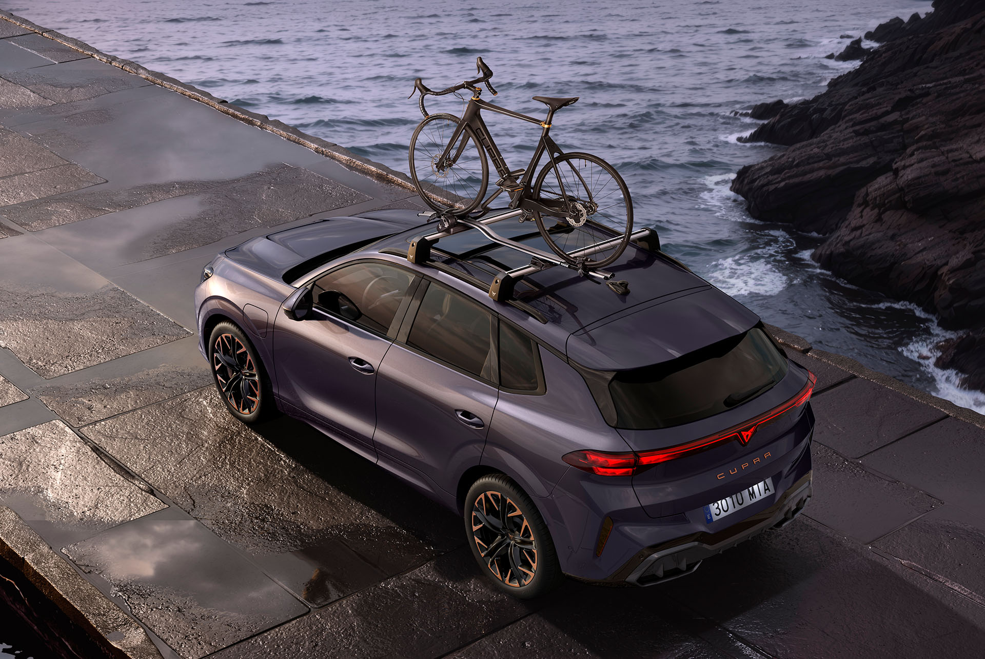 CUPRA Terramar amb portabicicletes transportant dues bicicletes. L'SUV està estacionat en una carretera costanera, mostrant la facilitat d'instal·lació del suport i el seu sistema antirobatori segur, preparat per a una aventura.